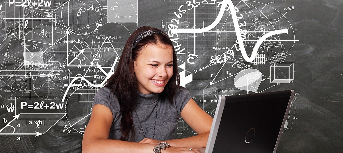 Ein Mädchen sitzt lächelnd vor einem Laptop, im Hintergrund sind Formeln und mathematische Zeichen zu sehen