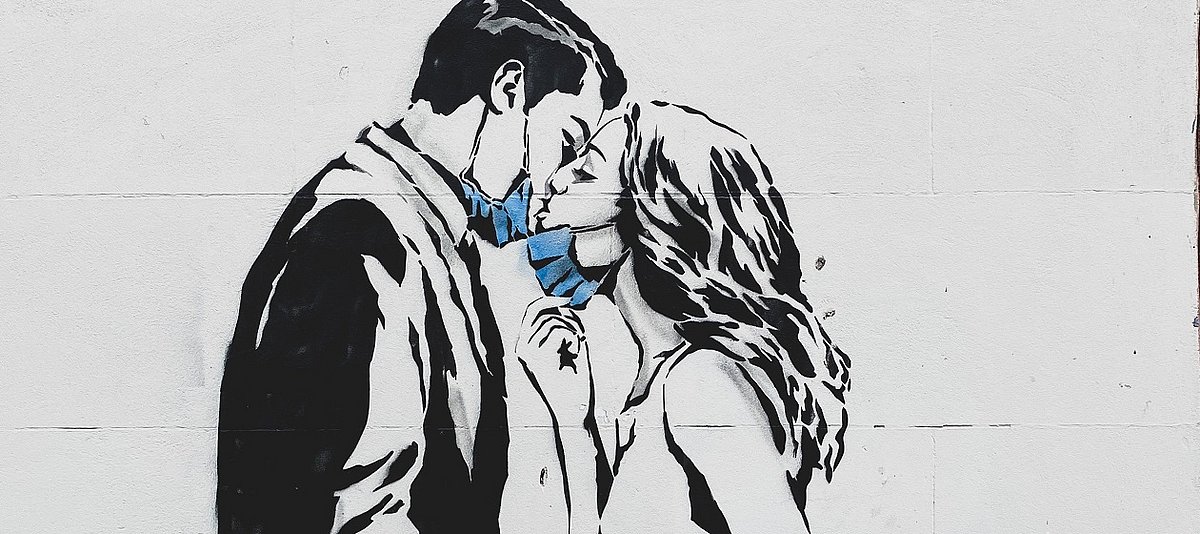 Graffiti von einem Mann und eine Frau mit heruntergezogener Mund-Nase-Bedeckung, die sich küssen