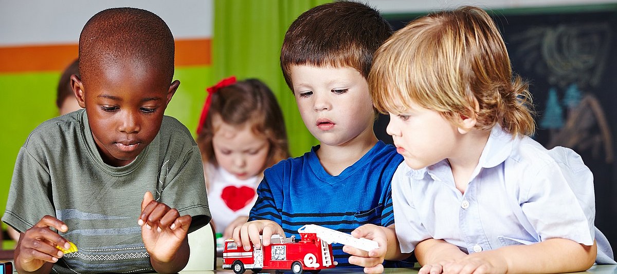 Drei Kinder beschäftigen sich im Kindergarten gemeinsam mit Spielzeugautos.