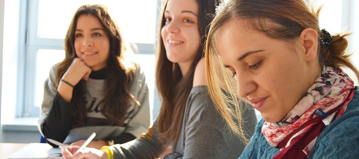 Drei Jugendliche sitzen in einer Unterrichtssituation und hören interessiert zu