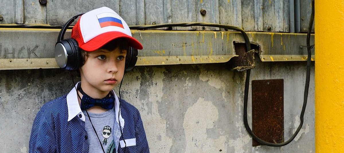 Ein Junge mit Kopfhörern sitzt an einer Mauer und schaut traurig