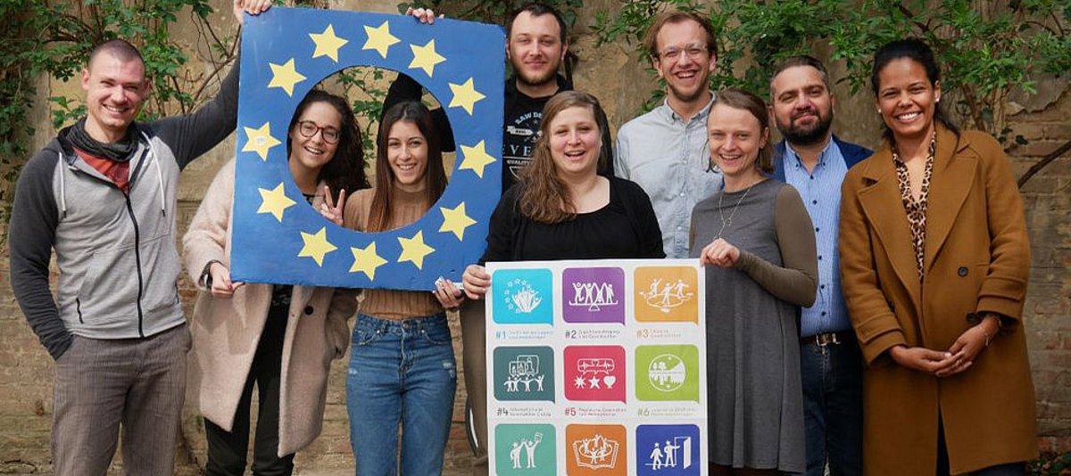 Die Teilnehmenden an dem Treffen halten zwei Posten mit den Youth Goals und einer Europafahne in der Hand.