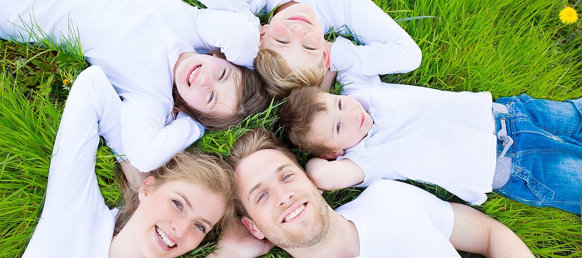Eltern und drei Kinder liegen auf einer Blumenwiese und schauen in den Himmel