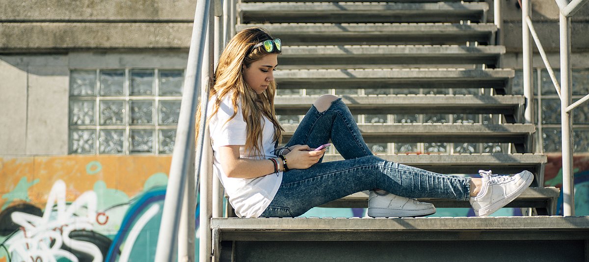 Jugendliche sitzt mit Handy auf einer Treppe