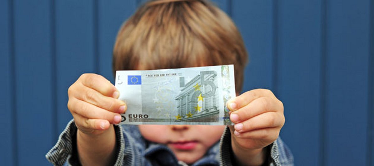 Ein kleiner Junge hält einen 5-Euro-Schein hoch