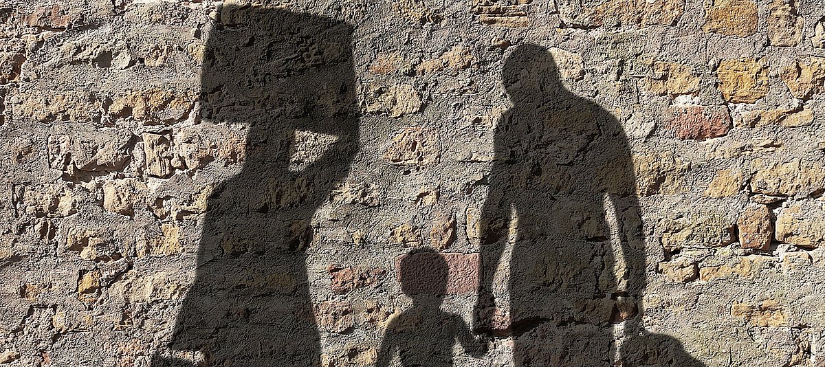 Eine Familie mit Gepäck ist als Schatten auf einer Mauer zu sehen.