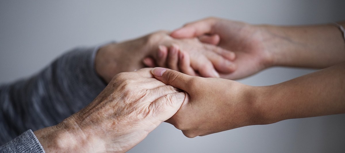 Junge Hände halten unterstützend die Hände einer älteren Person