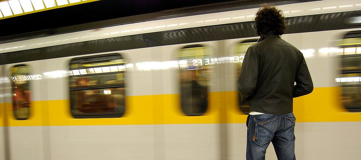 Mann steht am Bahnsteig vor einfahrender U-bahn