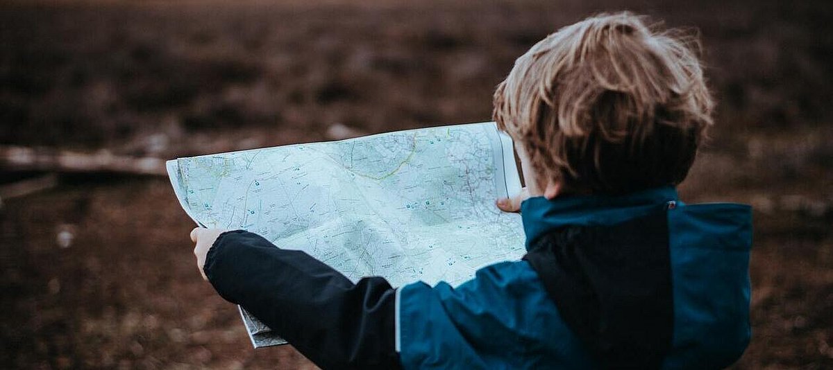 Ein Junge im blauen Anorak schaut auf die Landkarte in seinen Händen.