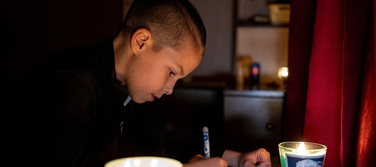 Auf dem Foto ist ein Kind zu sehen, das im Kerzenschein schreibt.