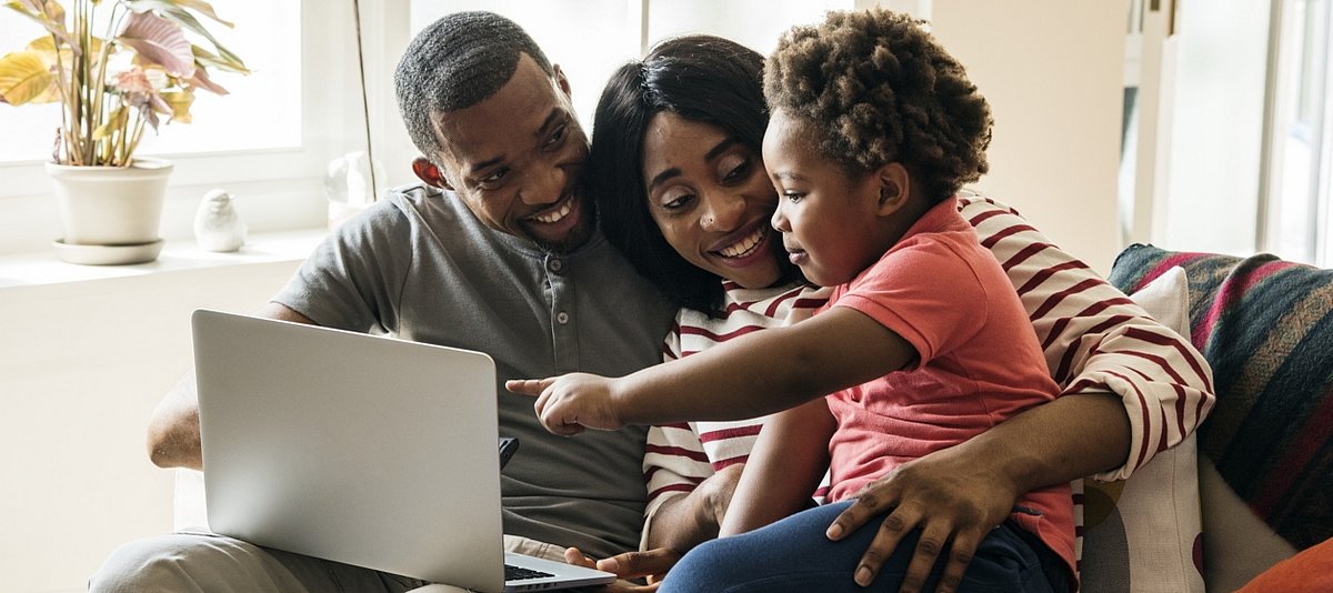 Eine Familie sitzt im Wohnzimmer und schaut sich mit der Tochter etwas auf dem Laptop an