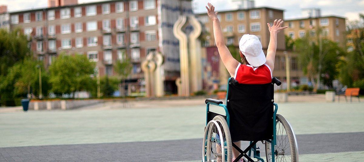 Ein Kind mit Baseballkappe sitzt in einem Rollstuhl und reckt die Arme in die Luft