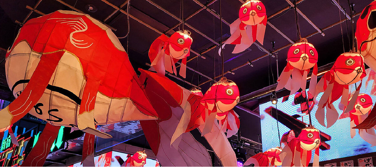 Rote Lampions in Fischform hängen von der Decke eines Raums